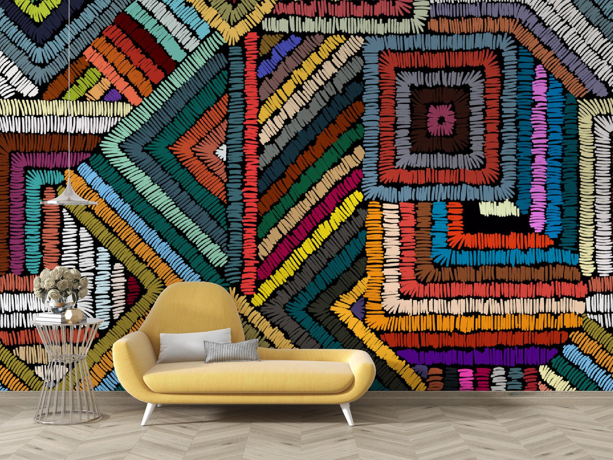 A vibrant, multicolored geometric wall mural with a textured, stitched or ribbed pattern, shown in a modern living room setting behind a yellow armchair and a small side table.