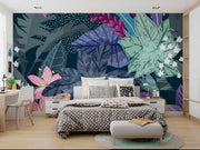 Illustrated tropical botanical wall mural with large jungle leaves, pink lilies, white flowers, and deep blue background, styled in a modern bedroom.