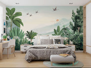 Scenic jungle wall mural with green tropical leaves, misty mountains, and flying cranes against a soft sunrise backdrop.