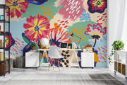 Vibrant floral wall mural with bold, hand-painted flowers in red, yellow, blue, and green, displayed in a modern home office setting.