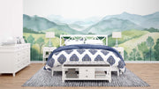 Watercolor green hills wall mural featuring lush rolling landscapes and soft blue mountains, styled in a cozy modern bedroom.