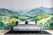 Watercolor green hills wall mural featuring lush rolling landscapes and soft blue mountains, styled in a cozy modern bedroom.