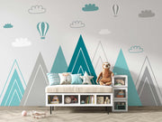 Modern geometric mountain wall mural in teal and grey with hot air balloons and clouds, styled in a contemporary nursery with a storage bench.
