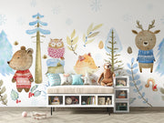Winter woodland animal wall mural featuring a bear, fox, deer, and owl in cozy knitted sweaters, surrounded by snow-covered trees and soft blue foliage.