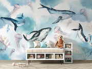 Underwater ocean wall mural with watercolor whales, jellyfish, and coral reefs in calming blue tones, displayed in a children's room with cozy decor.