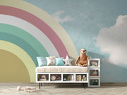 Kids playroom with retro pastel rainbow wall mural and sky backdrop, styled with minimalist white furniture and toys.
