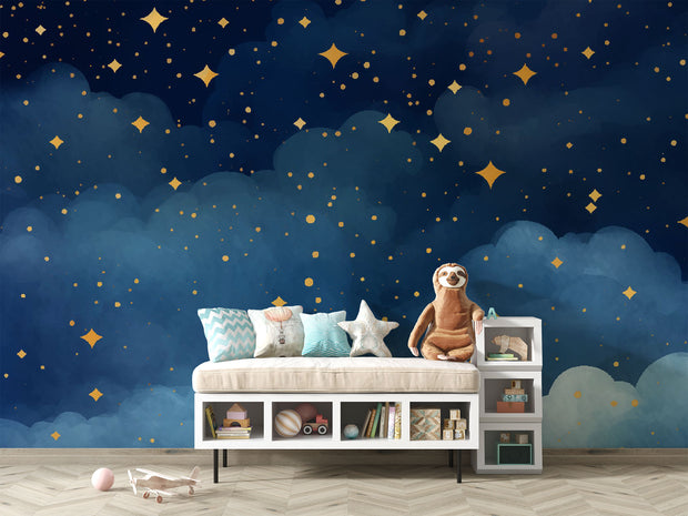 Starry night wall mural with golden stars and deep blue watercolor-style clouds, decorating a cozy bedroom with patterned bedding, soft toys and storage.