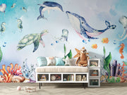 Underwater-themed kids wall mural with watercolor illustrations of a whale, turtle, dolphin, jellyfish, seahorses, coral, and fish in a nursery setting.