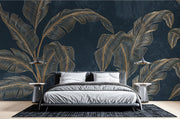 Golden banana leaf wall mural with metallic leaves on a deep black background, styled in a modern bedroom with a sleek bed and pendant lights
