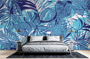 Tropical blue leaf wall mural featuring bold illustrations of large leaves in vibrant aqua and navy tones, decorating a modern bedroom with sleek furniture and cozy bedding.