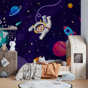 Cosmic explorer wall mural with cartoon astronaut, rocket ship, planets, and starry galaxy background in a playful kids’ bedroom.