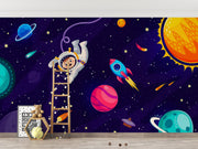 Cosmic explorer wall mural with cartoon astronaut, rocket ship, planets, and starry galaxy background in a playful kids’ bedroom.