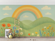 Pastel rainbow and floral landscape mural behind ladder and framed alphabet print in children’s playroom.