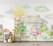 Pastel dinosaur wall mural with soft watercolor-style dinosaurs, a cozy stone cave, lush greenery, and a glowing sun, perfect for nurseries and playrooms.