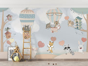 Nursery wall mural with pastel-colored forest animals flying in hot air balloons, surrounded by trees, clouds, and heart-shaped balloons