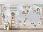 Nursery wall mural with pastel-colored forest animals flying in hot air balloons, surrounded by trees, clouds, and heart-shaped balloons