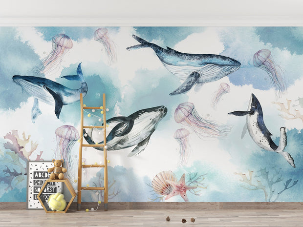 Underwater ocean wall mural with watercolor whales, jellyfish, and coral reefs in calming blue tones, displayed in a children's room with cozy decor.