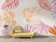 Colorful tropical leaf wall mural featuring overlapping monstera and palm leaves in soft orange, pink, and red tones, styled in a modenr living room.