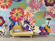 Vibrant floral wall mural with bold, hand-painted flowers in red, yellow, blue, and green, displayed in a modern living room setting.