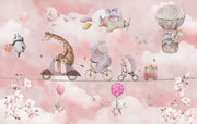 A whimsical nursery wall mural featuring playful animals, including a giraffe on a scooter, an elephant on a bike, and a panda floating with balloons over pink clouds.