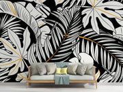 Black and white tropical leaf wall mural with gold accents, featuring monstera and palm leaves in a modern botanical design.