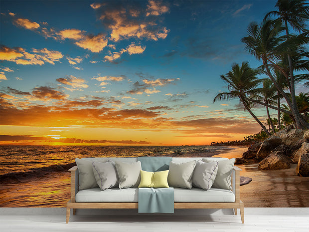 Golden sunset wall mural with palm trees, vibrant sky, and tranquil ocean waves, creating a relaxing and coastal living room ambiance.