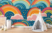 Bold and colorful rainbow wall mural with pink clouds and blue background, decorating kids playroom.