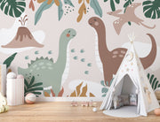 Kids’ wall mural with cartoon dinosaurs, volcano, pterodactyl, and tropical leaves in soft earth tones; styled in a cozy children’s playroom.