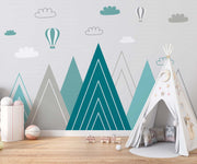 Modern geometric mountain wall mural in teal and grey with hot air balloons and clouds, styled in kids' play room.