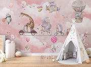 A whimsical nursery wall mural featuring playful animals, including a giraffe on a scooter, an elephant on a bike, and a panda floating with balloons over pink clouds.