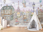 A whimsical Paris-inspired nursery wall mural featuring teddy bears on scooters and bikes, cobblestone streets, and the Eiffel Tower in pastel tones.