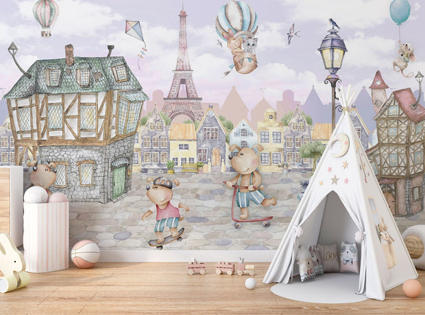 A whimsical Paris-inspired nursery wall mural featuring teddy bears on scooters and bikes, cobblestone streets, and the Eiffel Tower in pastel tones.