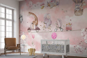 A whimsical nursery wall mural featuring playful animals, including a giraffe on a scooter, an elephant on a bike, and a panda floating with balloons over pink clouds.
