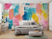 Colorful abstract wall mural with brushstroke patterns in vibrant pink, blue, yellow, and coral shades, installed behind a modern bed setup.