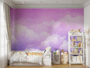Dreamy cloud-themed wall mural with soft purple hues and fluffy white clouds, decorating a modern children's room with cosy accents and toys.