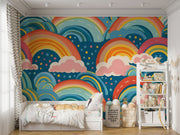 Bold and colorful rainbow wall mural with pink clouds and blue background, decorating kids playroom.
