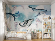 Underwater ocean wall mural with watercolor whales, jellyfish, and coral reefs in calming blue tones, displayed in a children's room with cozy decor.