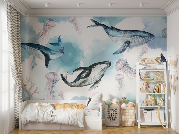Underwater ocean wall mural with watercolor whales, jellyfish, and coral reefs in calming blue tones, displayed in a children's room with cozy decor.