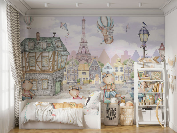 A whimsical Paris-inspired nursery wall mural featuring teddy bears on scooters and bikes, cobblestone streets, and the Eiffel Tower in pastel tones.
