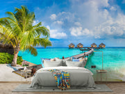 Tropical paradise wall mural with overwater bungalows, palm trees, turquoise sea, and a wooden pier, creating a serene and exotic room atmosphere.