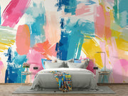 Colorful abstract wall mural with brushstroke patterns in vibrant pink, blue, yellow, and coral shades, installed behind a modern bed setup.