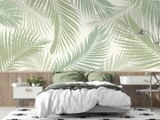 Serene palm leaf wall mural with soft green overlapping leaves on a neutral background, styled in a modern bedroom with wooden accents.