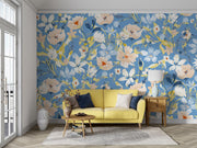 Bold botanical wall mural with vibrant blue, beige, and yellow flowers, styled in a modern living room with a yellow sofa.