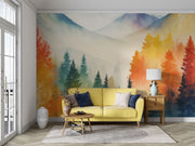 Watercolor mountain landscape wall mural with autumn forest in orange, yellow and teal, styled in living room with yellow sofa.
