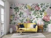 Elegant vintage floral wall mural with pink roses, lilacs, and greenery behind a yellow sofa in a cozy, light-filled living room.