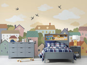 Whimsical village wall mural featuring pastel houses, trees, clouds, and flying birds, styled in a cozy and creative kids’ playroom.