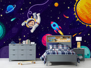 Cosmic explorer wall mural with cartoon astronaut, rocket ship, planets, and starry galaxy background in a playful kids’ bedroom.