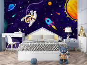 Cosmic explorer wall mural with cartoon astronaut, rocket ship, planets, and starry galaxy background in a playful kids’ bedroom.