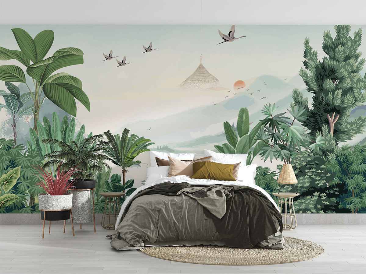 Scenic jungle wall mural with green tropical leaves, misty mountains, and flying cranes against a soft sunrise backdrop.