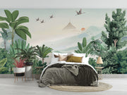 Scenic jungle wall mural with green tropical leaves, misty mountains, and flying cranes against a soft sunrise backdrop.
